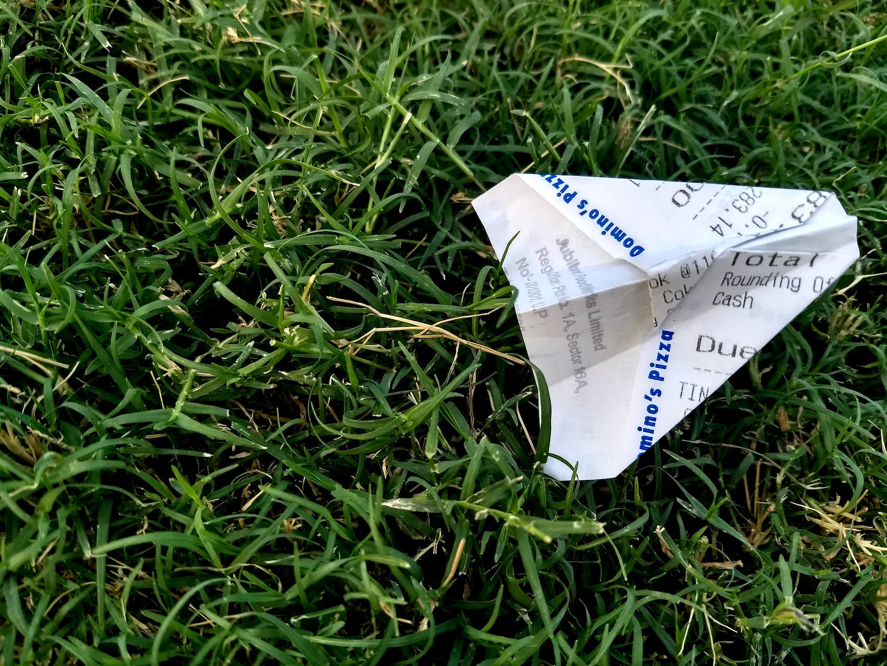 receipt folded into paper plane on grass